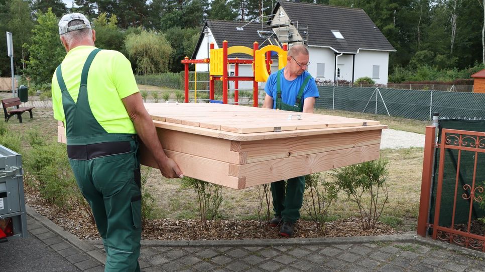 Bauhofmitarbeiter setzen den Sandkasten an seinen Bestimmungsort.